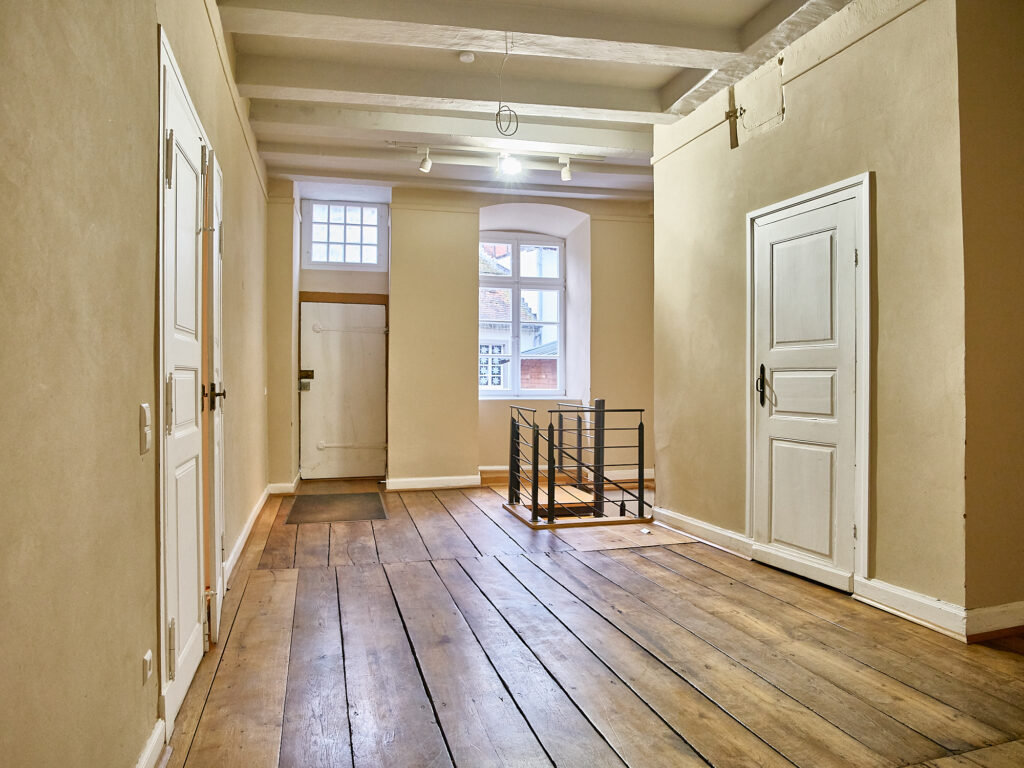 Heller Flur mit historischen Holzdielen und Zugang zu Salon und Nebenräumen.